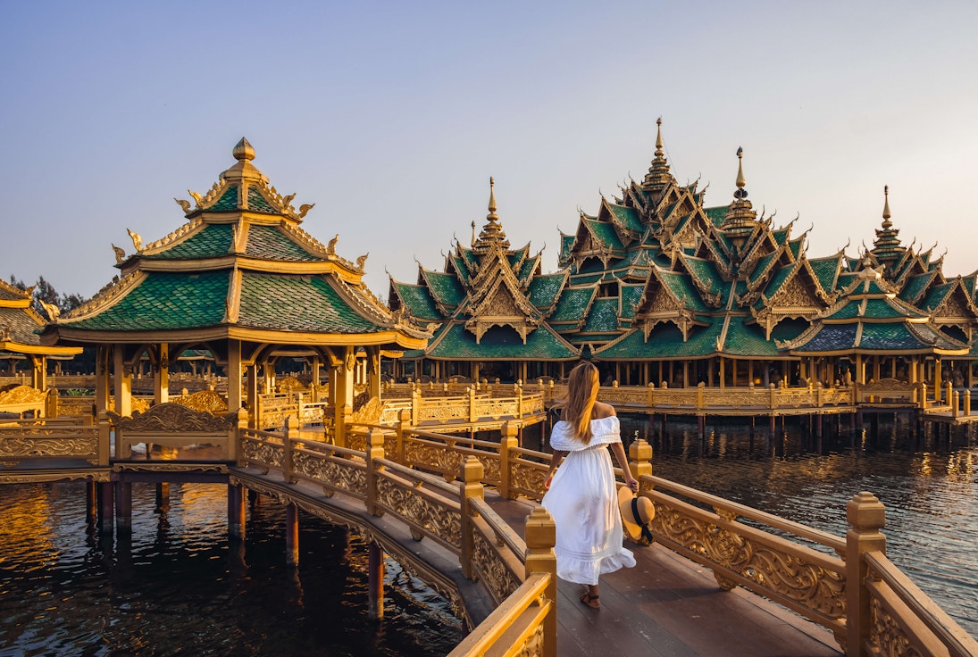 Woman walking on a bridge to Buddhist temple in Thailand during sunset.