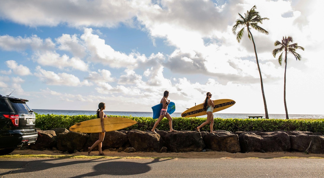 Pacific Islander surfers carry their boards to the water.