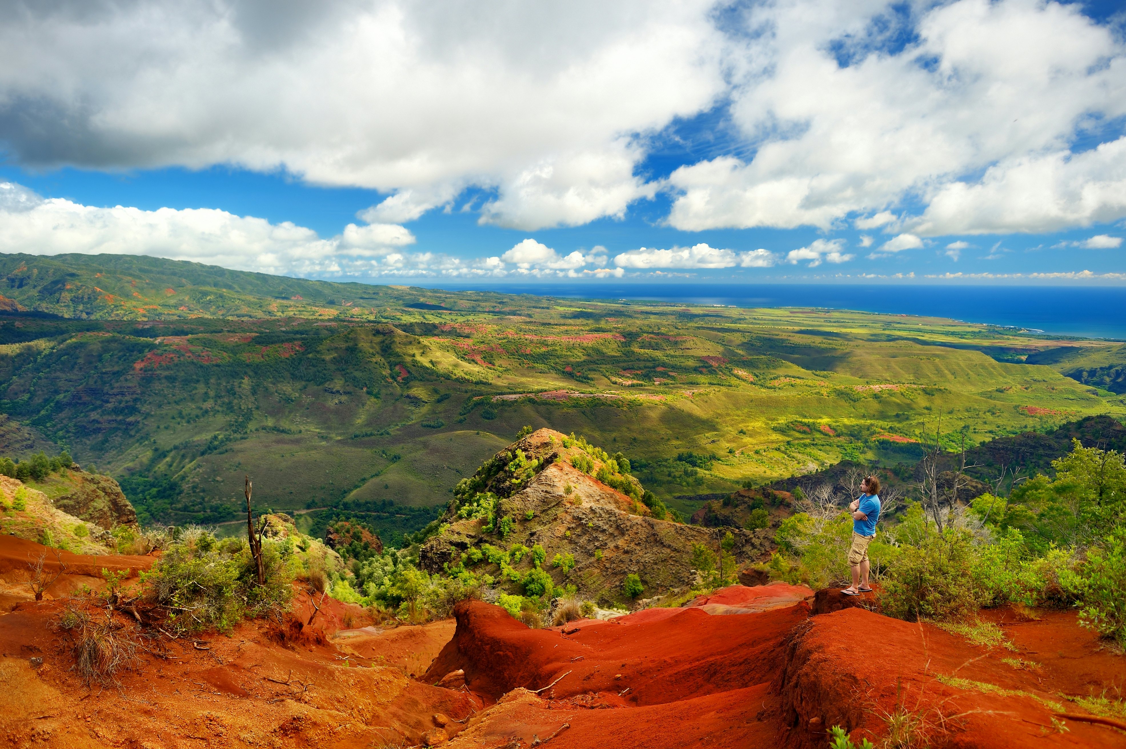 A hiker gazes down upon a landscape with many different valleys within it as clouds gather in the distance