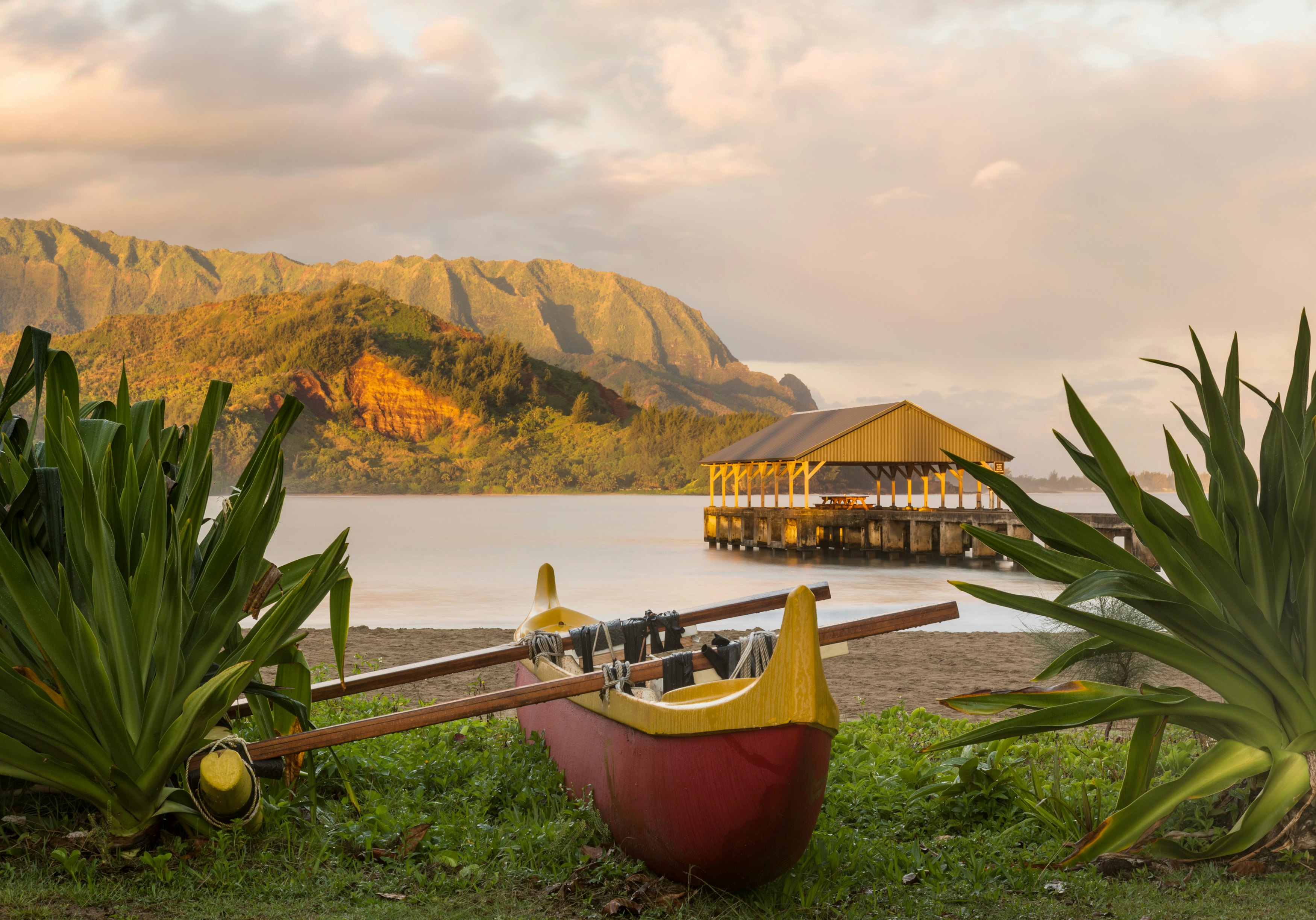 Red and yellow hawaiian canoe with outrigger on the beach at Hanalei pier at dawn as the sun lights the sky over Na Pali mountains
179311358
sky, bay, sea, calm, pier, shed, dawn, boat, coast, kauai, kayak, beach, jetty, ocean, island, nobody, travel, clouds, scenic, hawaii, coastal, sunrise, pacific, walkway, tropical, dramatic, paradise, relaxing, mountain, seascape, peaceful, beautiful, coastline, landscape, pali, canoe, hanalei, hawaiian, na