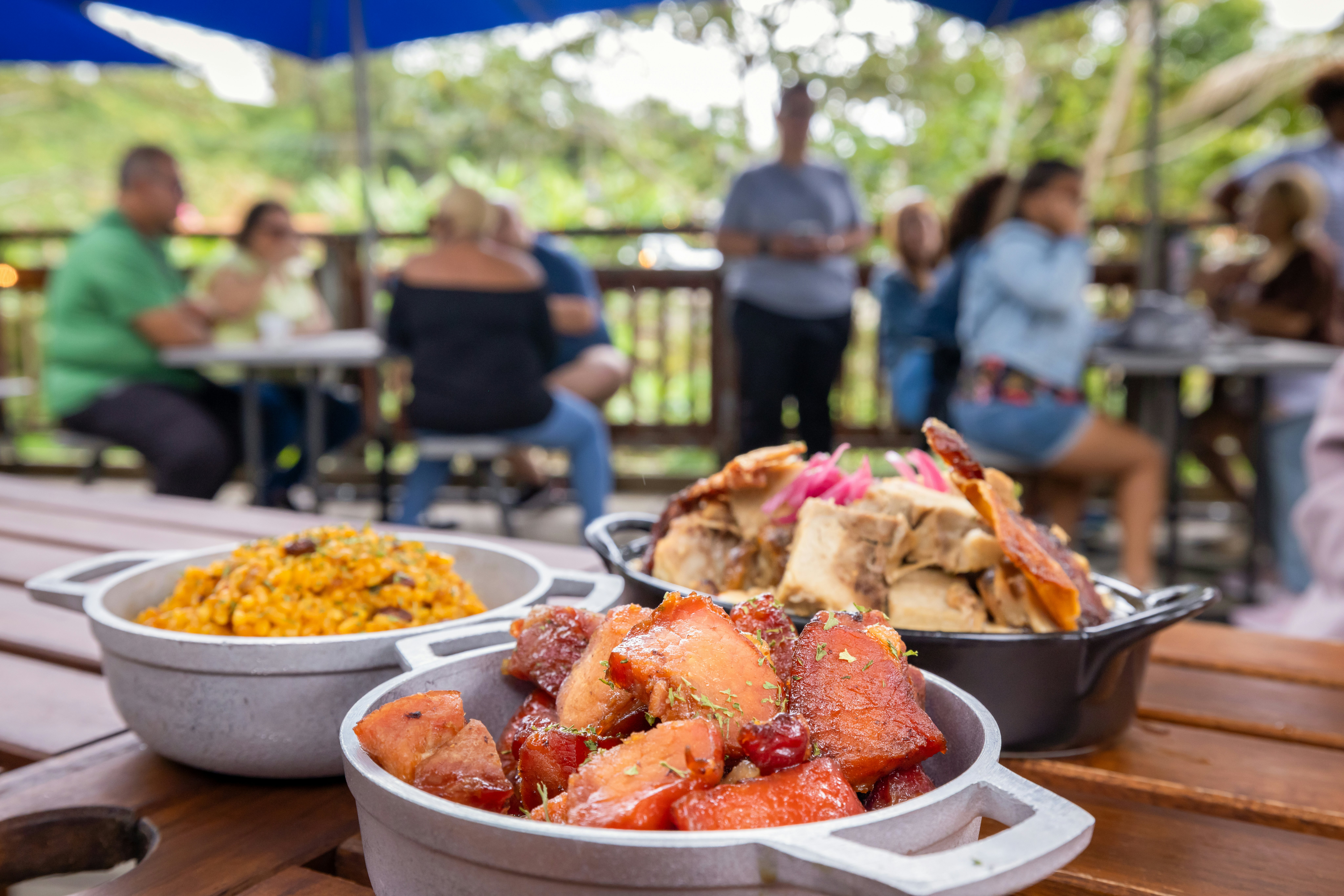 A smoked meat dish accompanied by a bowl of rice and mac and cheese on a wooden table in a busy restaurant