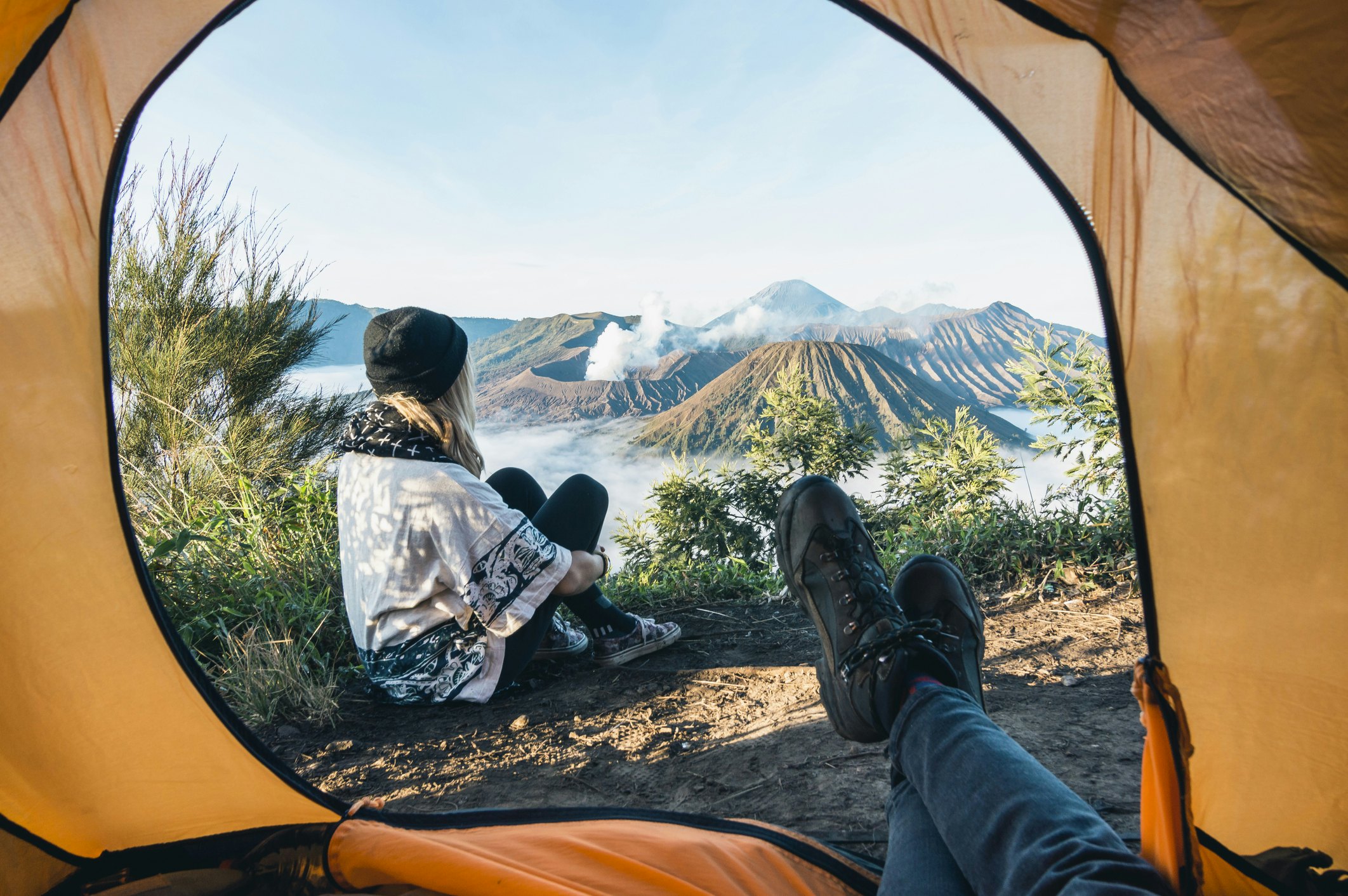A woman sits with their back to a tent looking out over a volcanic landscape