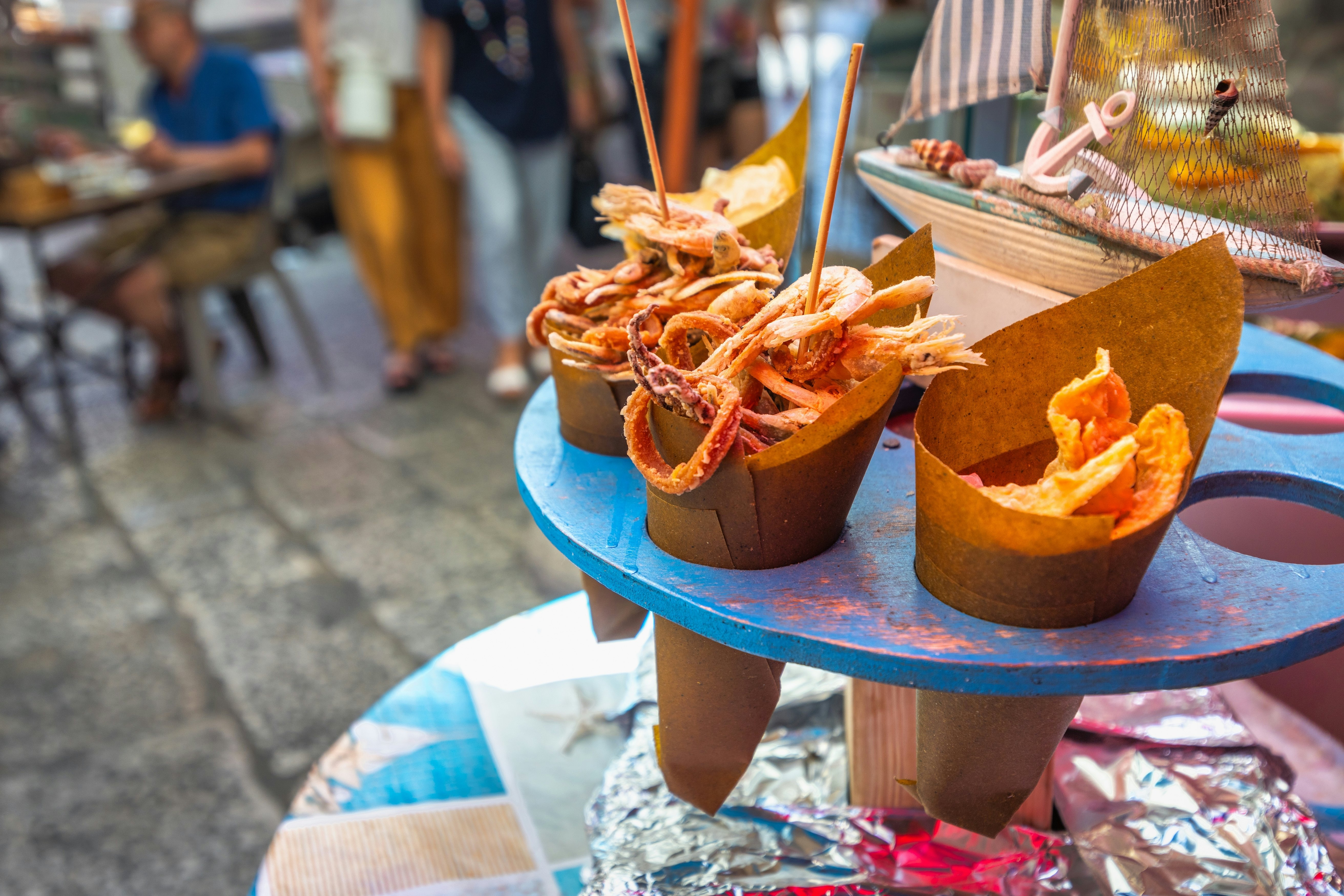 Fried seafood in brown paper cones sit on a blue rack.