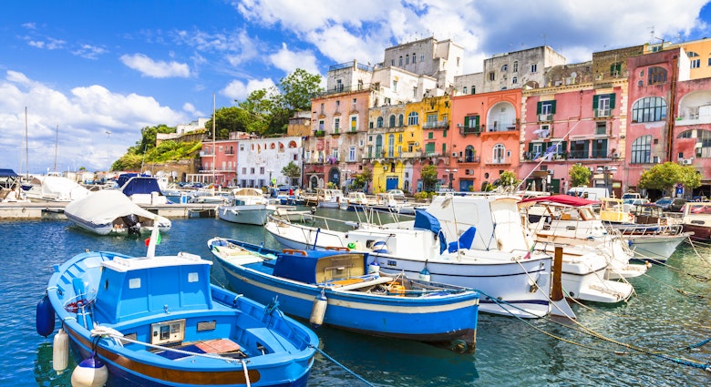 Colourful fishing boats, sitting side by side, bob in the marina in the foreground, while the vibrant pink and yellow buildings stand in the background.