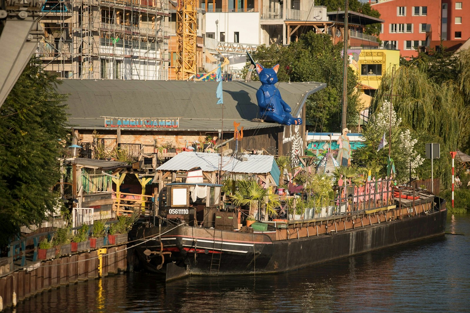 A riverside village and moored barge with a large blue cat sculpture sat on a rooftop