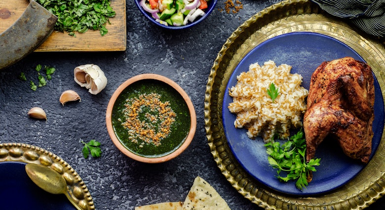 Egyptian dish of molokhiyya placed with rice, chicken, pita bread and green salad.