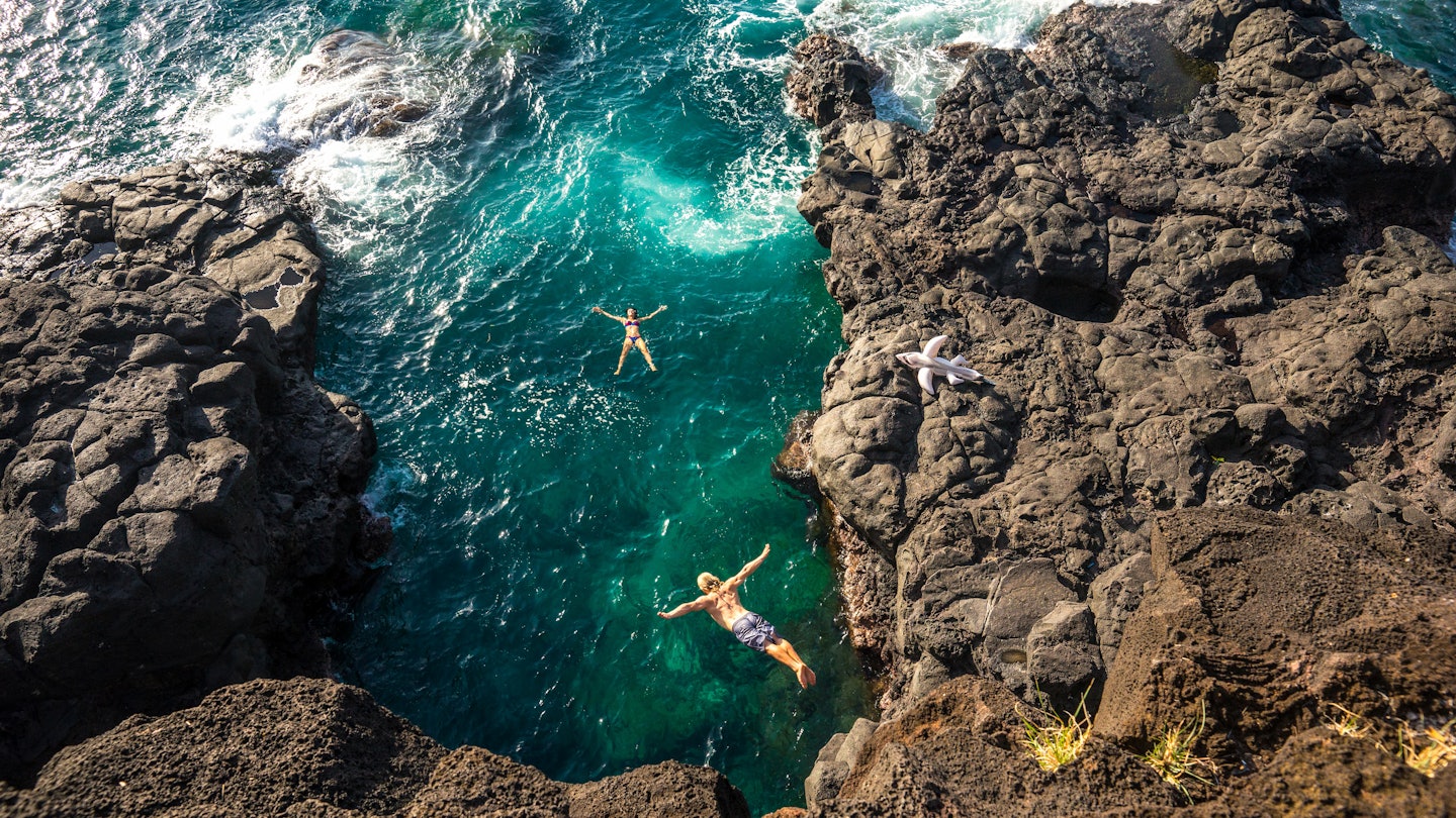 Young muscular guy jumping from a high cliff into the clear ocean on the island of Mauritius. Girl model bathes in the ocean and looking at the bottom of his jump, License Type: media, Download Time: 2025-01-30T21:21:24.000Z, User: rhylton_redventures, Editorial: false, purchase_order: 56530 - Guidebooks, job: Lonely Planet WIP, client: Lonely Planet WIP, other: Rhianydd Hylton